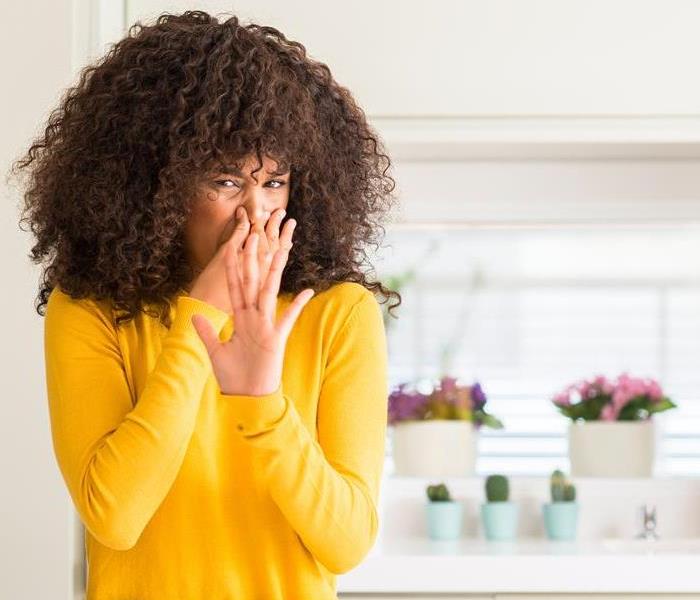 woman wearing yellow sweater at kitchen smelling something stinky