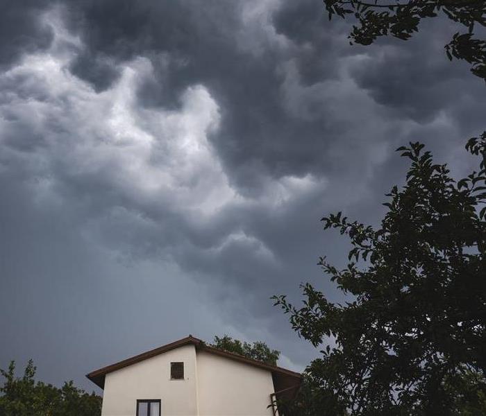 Dramatic stormy sky above the roof of a house with branches of a tree on the right